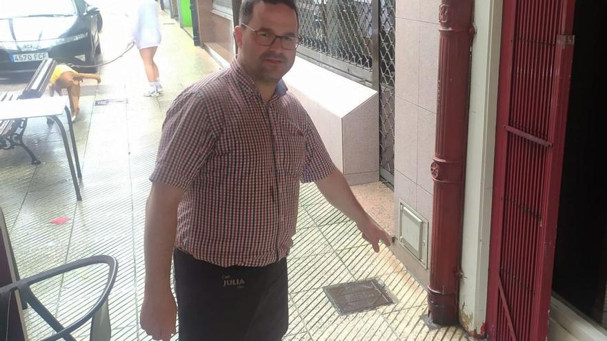 Fernando González, a la puerta de su local, señala desperfectos en la verja producto del pis de los perros, mientras, a su espalda y de modo casual, una mascota orina junto a un banco.