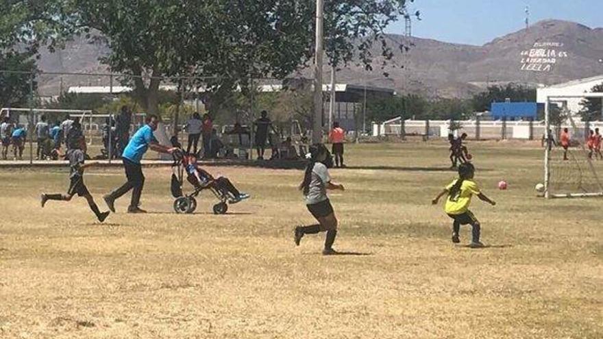 Un padre empuja la silla de ruedas de su hijo para que pueda jugar al fútbol