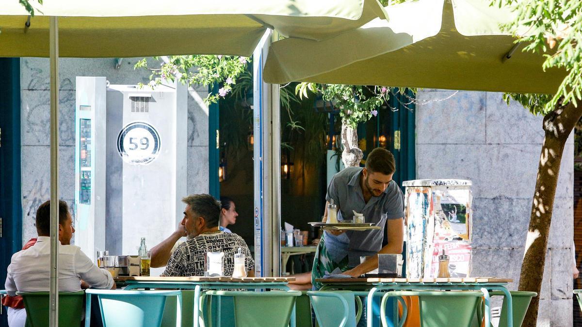 Un camarero limpia las mesas de la terraza de una cafetería.