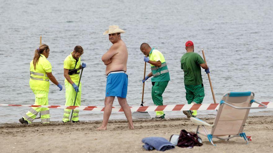 Turistas observan como operarios de La Línea retiran restos de aceite de la Playa de Poniente.