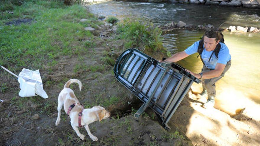 Un voluntario retira una silla del cauce del río Mero. / Víctor Echave