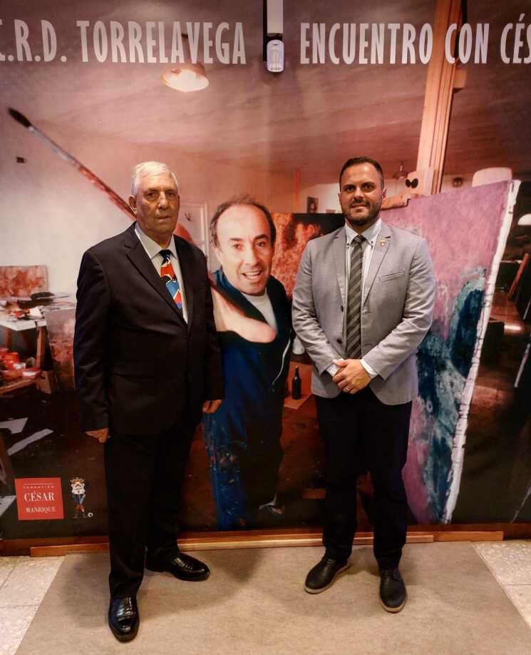Toñín Ramos (i) y Jonathan de León junto al cartel de la exposición Encuentro con César Manrique en la Sociedad Torrelavega por el 75 aniversario de la entidad