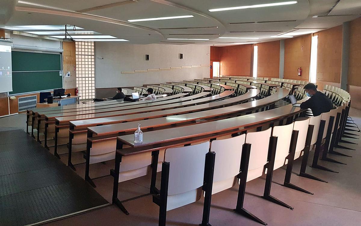 Clase semipresencial de introducción a la microeconomía, en el Aulario 1 de la UA, con la pantalla virtual a la izquierda de la pizarra.