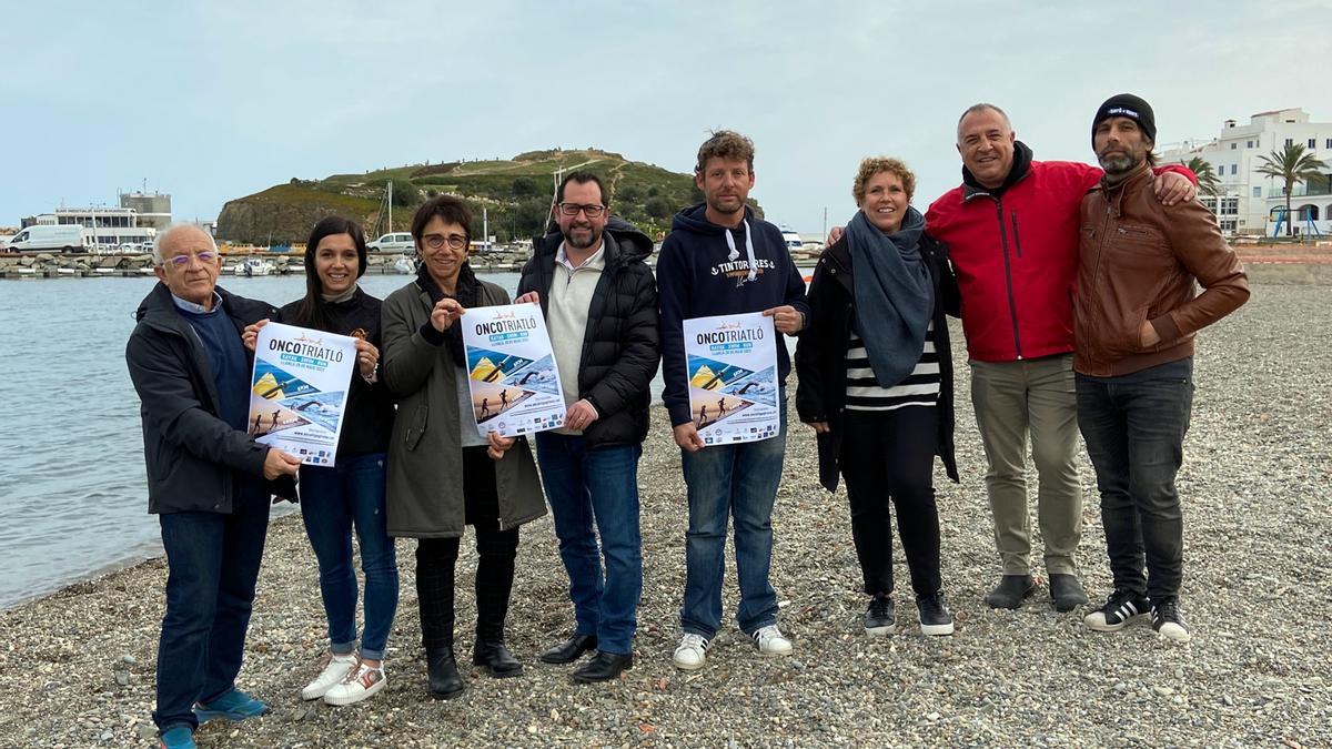 Els organitzadors de l&#039;Oncotriatló, amb el cartell de la prova esportiva, a la platja que hi ha al costat del port de Llançà