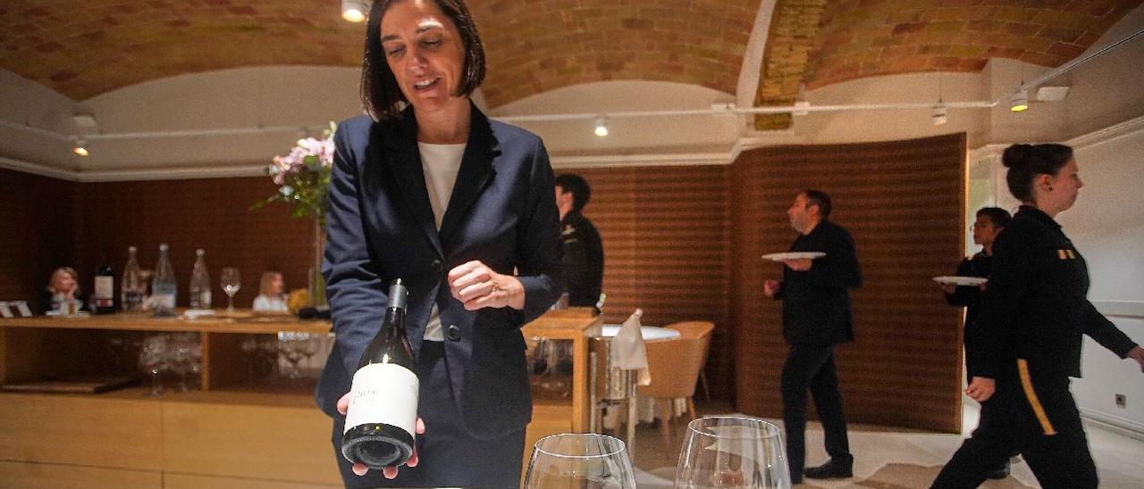 Laura Tejero, cap de sala i copropietària del restaurant Divinum de Girona, mostra un vi a uns comensals mentre al seu darrere diversos membres de l’equip porten plats a una altra taula.