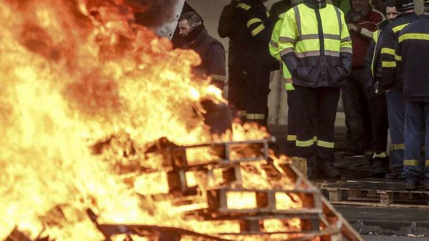 Un trabajador de Alcoa mira meditabundo cómo arde una pira de madera prendida delante de la fábrica en una pasada movilización