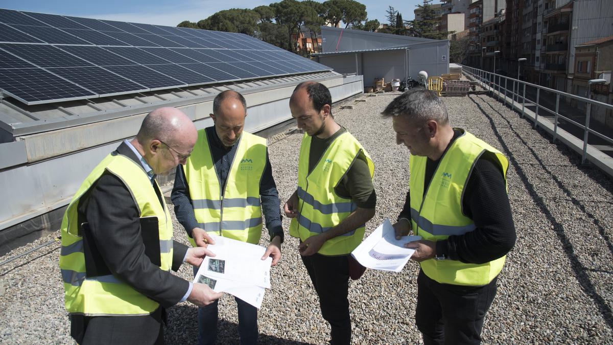 Ventura, Aloy, Huguet i Zaragoza, d'esquerra a dreta, consulten uns plànols davant d'un dels camps fotovoltaics instal·lats al terrat de les piscines municipals