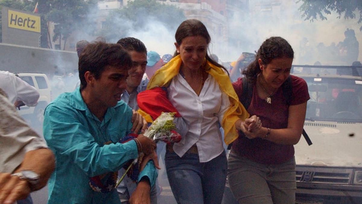 La opositora María Corina Machado, acompañada por simpatizantes, escapa de los gases lacrimógenos lanzados por la policía, este martes en Caracas.