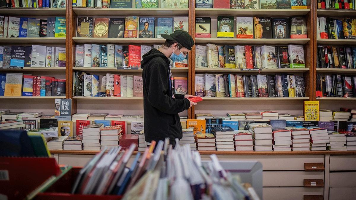 Un joven con mascarilla hojea un libro en una papelería-librería de Barcelona