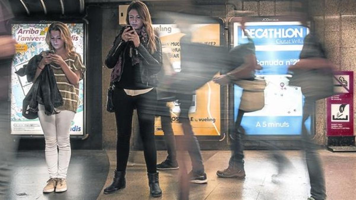 Jóvenes consultando su móvil en una estación de metro.