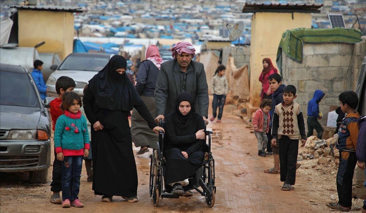 Una mujer siria discapacitada de la provincia de Hama es empujada en una silla de ruedas a través de un camino embarrado después de una lluvia torrencial que afectó a un campamento para personas desplazadas cerca de la ciudad de Atme, en la frontera con Turquía en la provincia de Idlib del norte, en su mayoría rebelde.
