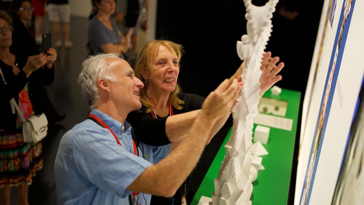 Un arquitecto de las obras del templo dirige la mano de una invidente en una maqueta de una de las torres.