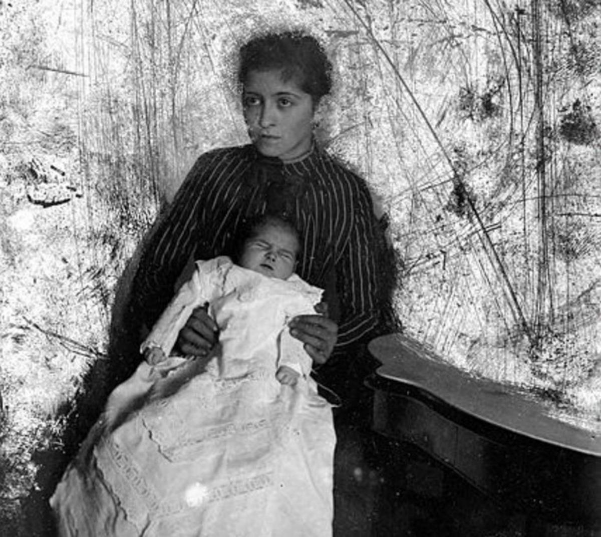 Retrato de estudio de una mujer con un niño en el regazo, vestido con ropa de bautizo. Colección de Baltasar Cue. | Fondos Muséu del Pueblu d’Asturies
