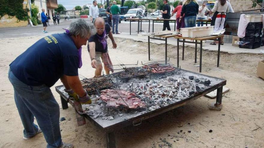 Varias personas preparan la parrillada para los vecinos de San Frontis.