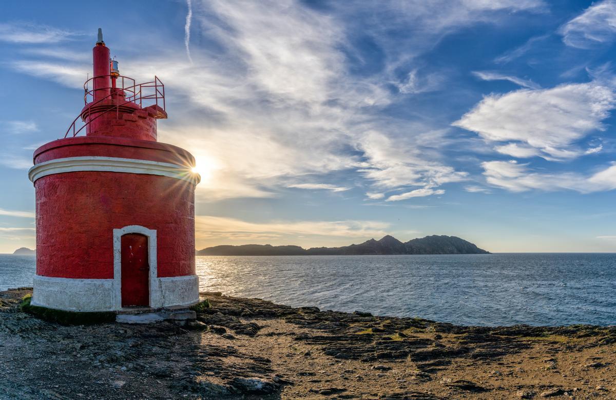 El sol dorado detrás del faro de Punta Robaleira en Galicia y las Islas Cíes detrás.