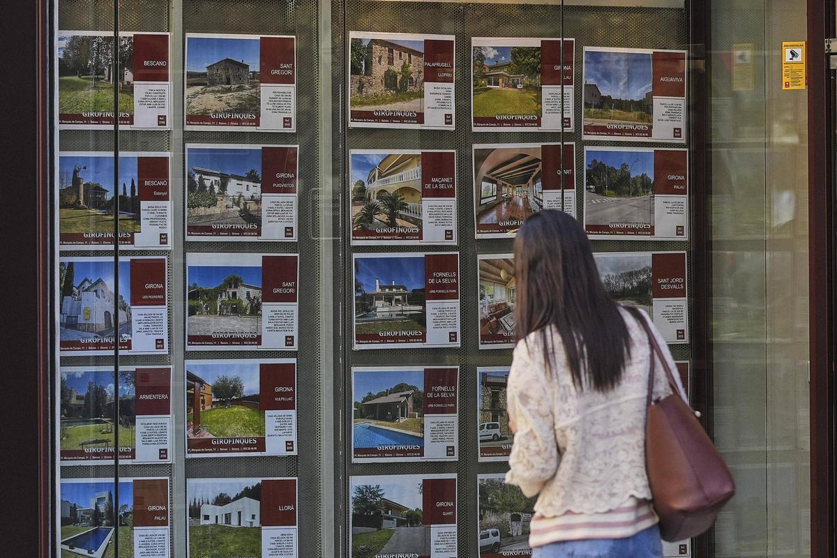 Una persona davant l'aparador d'una immobiliària a Girona consultant els anuncis.