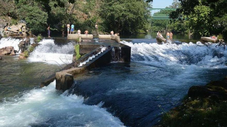 Varios bañistas se refrescan en la presa de Monte Porreiro, donde el río Lérez presenta un elevado nivel de agua.