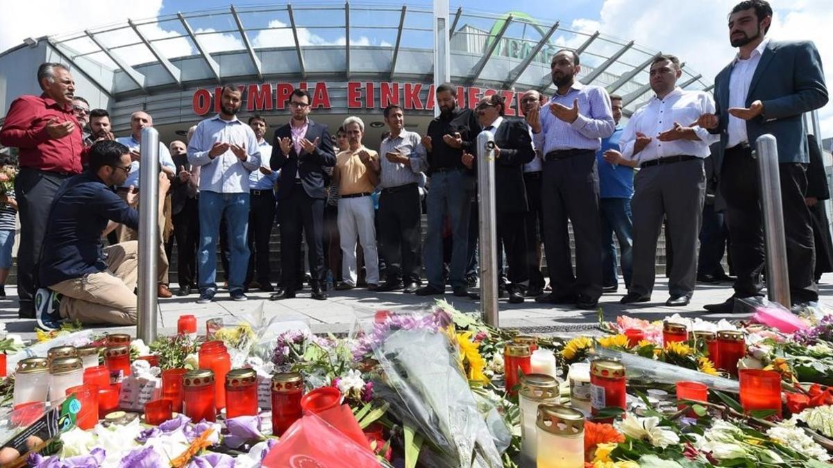 Varias personas rezan en el memorial de velas y flores, colocada frente al centro comercial Olympia, en Munich, este domingo.