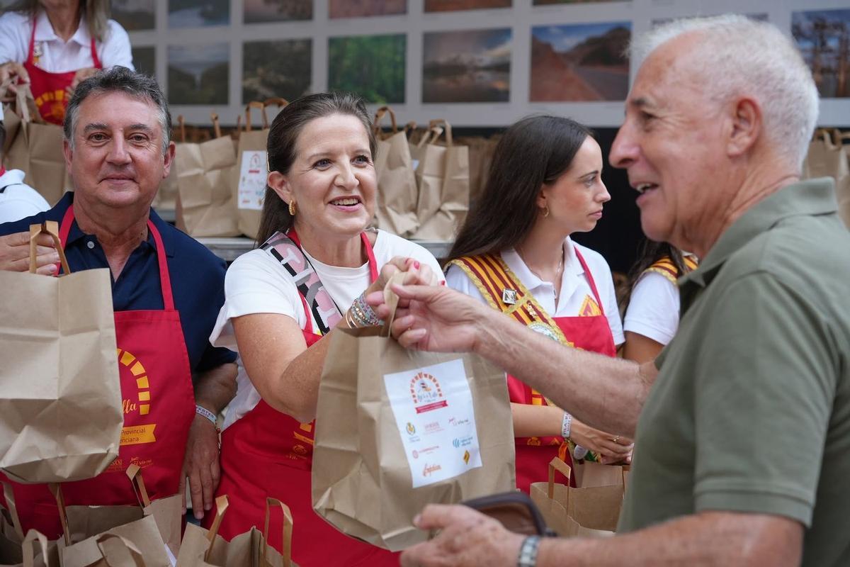 La presidenta de la Fundació Caixa Rural Vila-real dona a un veí una de les bosses amb el morter i els ingredients per a fer l'allioli,s