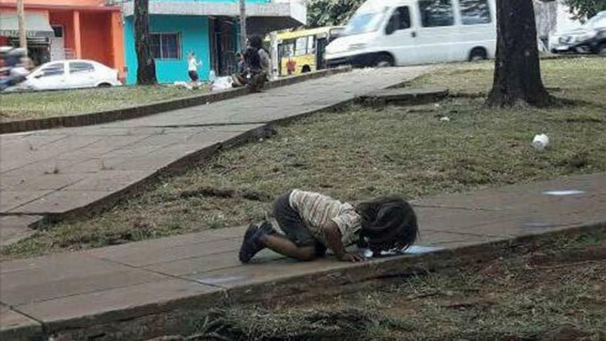 niño guaraní bebe de un charco de la calle