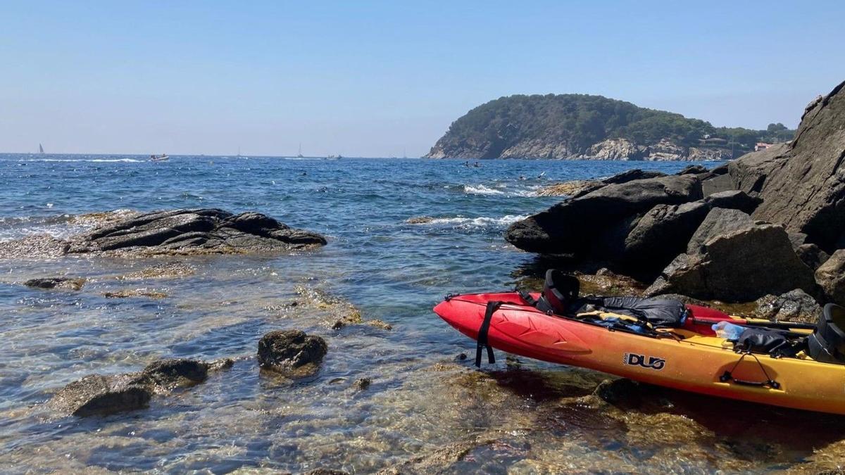 Un caiac reposa en una cala de Palamós, amb el Cap Gros de fons.