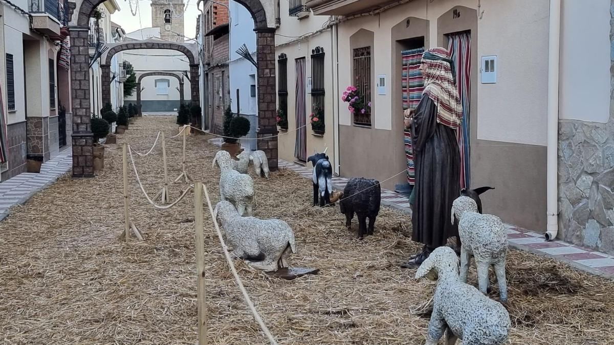 Con la iglesia al fondo, varios corderos simulan avanzar hacia adelante bajo la atenta mirada de una mujer.