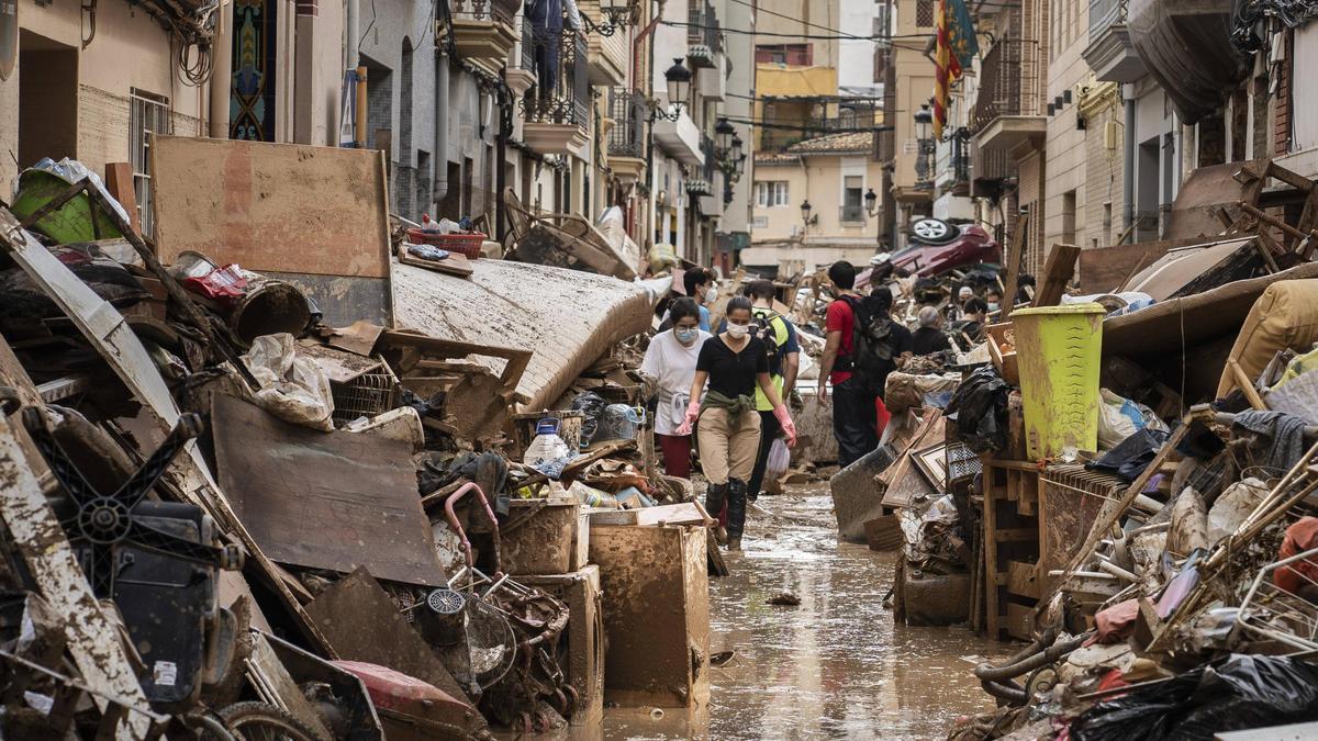 Voluntarios y vecinos avanzan entre montañas de muebles, colchones y residuos. Al fondo, un coche.