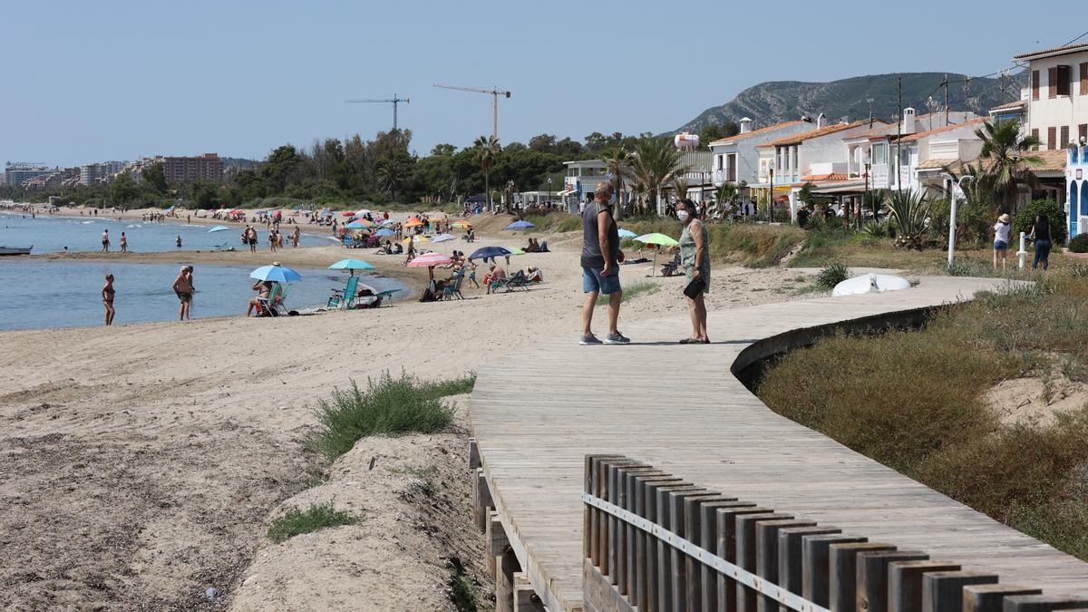 Dos personas pasean por la pasarela de la playa de Torre la Sal, con decenas de bañistas, en una foto de archivo.