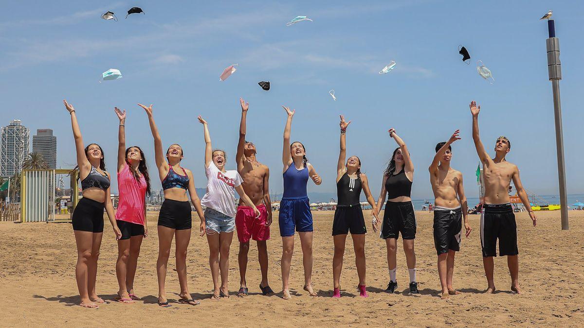 Unos jóvenes, en una playa de Barcelona, lanzan al aire las mascarillas.