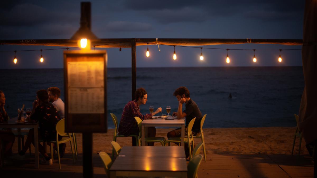 Dos jóvenes en la terraza de un restaurante, frente a la playa