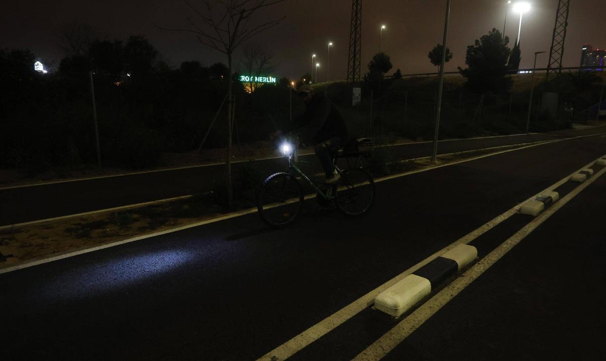 Un ciclista circula por el carril bici con la única luz del foco de su bicicleta.