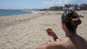 Una joven fuma en la playa del Pla de l’Ós en Premià de Mar.