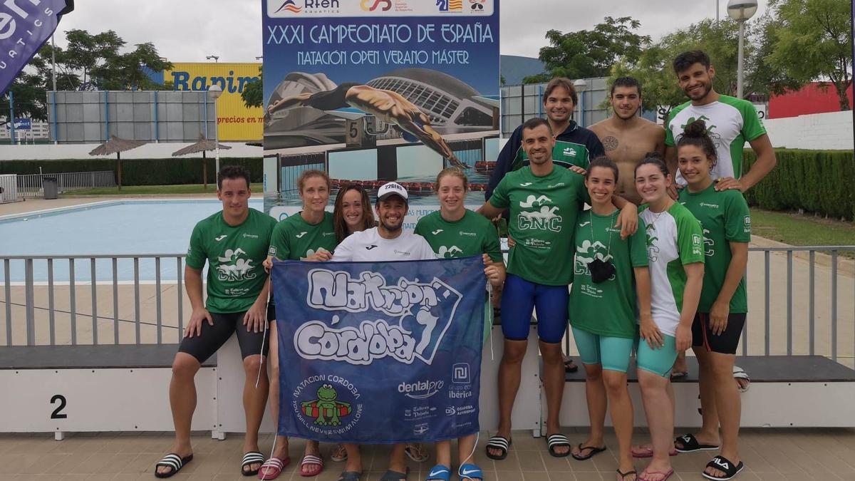 Nadadores del Natación Córdoba participantes en el Campeonato de España con Pedro Serrano de blanco sosteniendo el cartel del club.