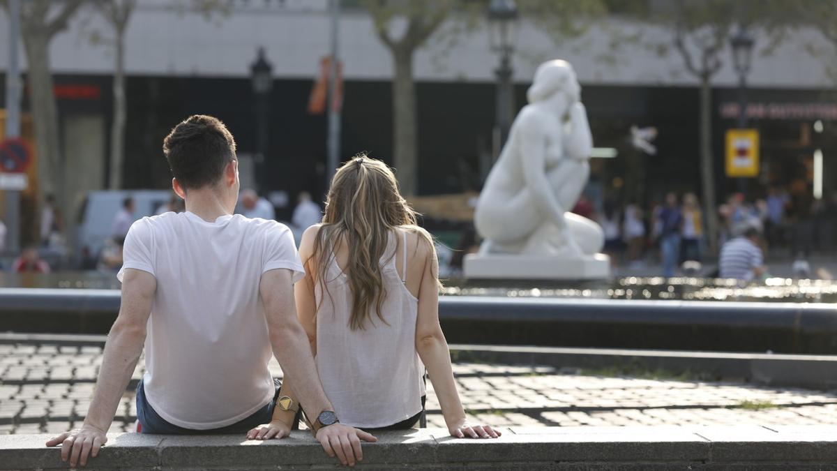 Una pareja, sentada sobre el poyo de una fuente en Barcelona.