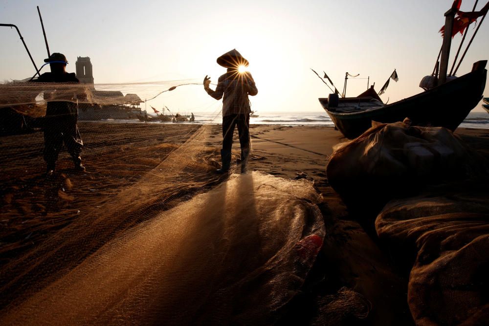 Fishermen clean their nets at a beach in Nam ...