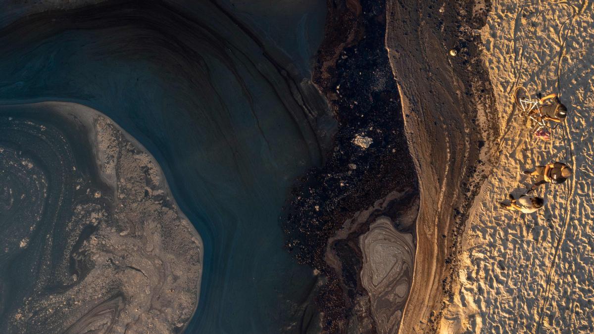 Esta fotografía aérea muestra a personas mirando el petróleo contra una berma de arena para evitar que fluya desde el océano hacia el río Santa Ana.