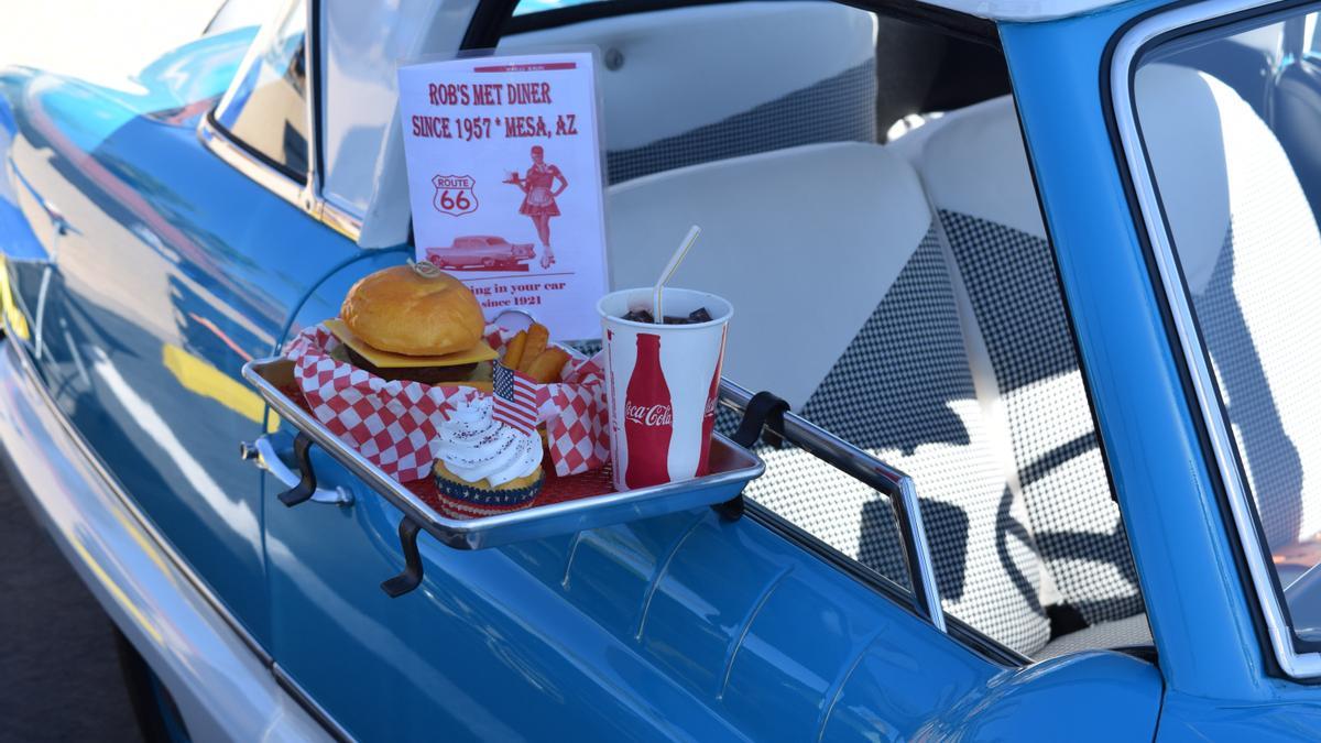 Un coche con bandeja de comida, hamburguesa y bebida, en el autocine