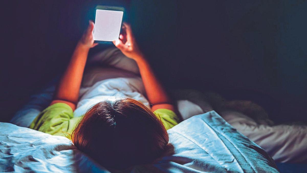 Un nen consultant un telèfon mòbil estirat al llit