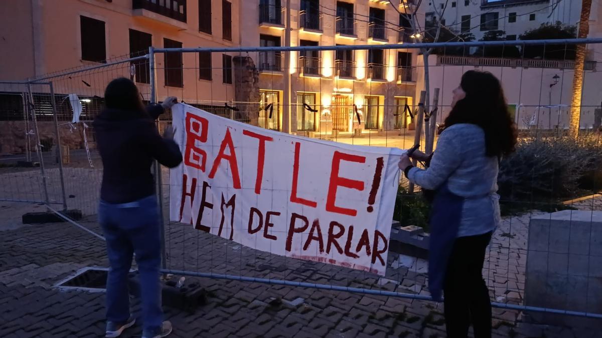 Dos vecinas cuelgan un cartel en la plaza Llorenç Villalonga.