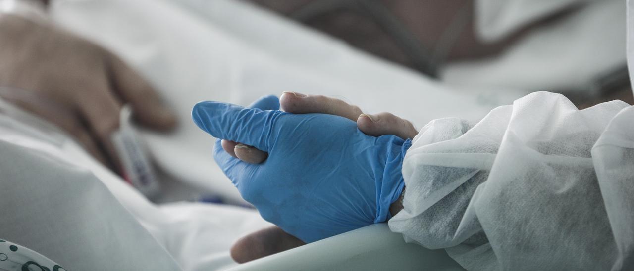 Un sanitario da la mano a un paciente en la UCI del Hospital de Son Espases