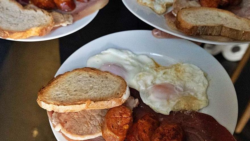 Un camarero lleva tres plato de dos y pingada a una mesa.