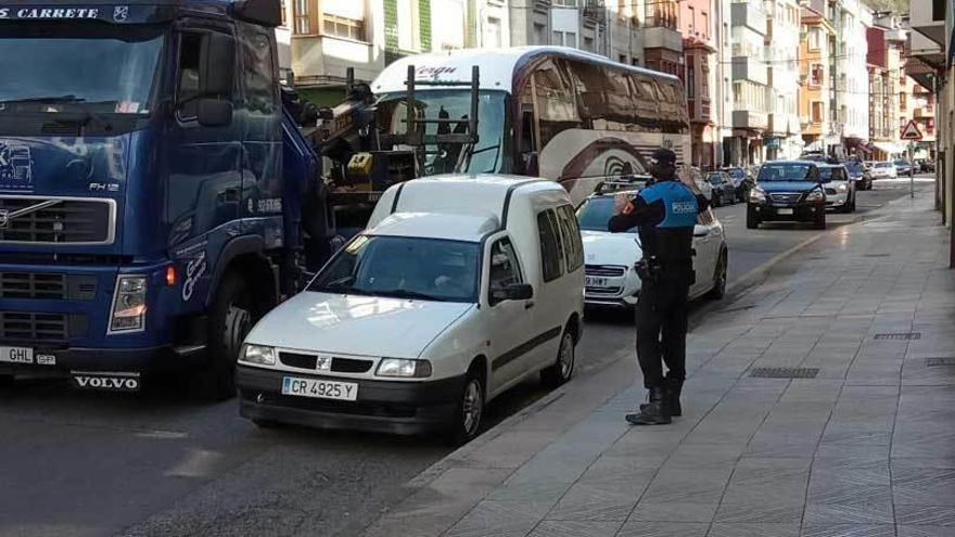 Un policía local regula el tráfico en el momento que una grúa procede a la retirada del autobús.