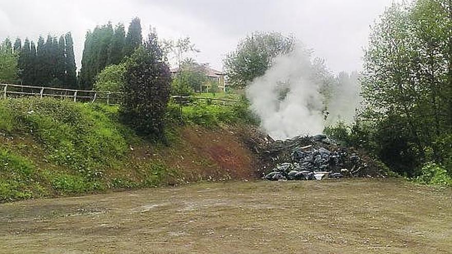 El montón de basura, en plena combustión, junto al vallado de la pista polideportiva de Candás.