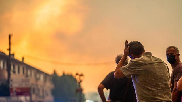 Diverses persones observen el foc durant les tasques d’extinció d’un incendi forestal.