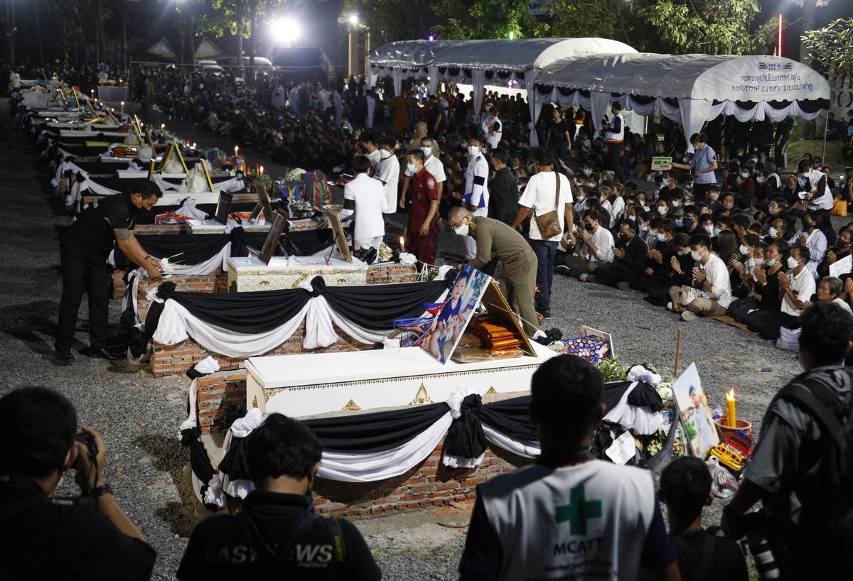  Funcionarios tailandeses depositan flores de sándalo sobre los ataúdes de las víctimas del tiroteo masivo en las piras funerarias 