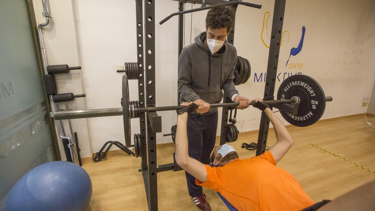 Dos usuarios de un gimnasio realizan ejercicio con mascarillas