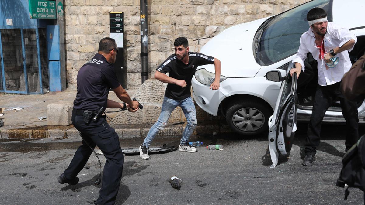 Jerusalem (--), 10/05/2021.- An Israeli policeman (L) points a gun at a Palestinian man (C) next to a wounded Orthodox Jewish man (R) who crashed his car near the Lions' Gate, as clashes continue at the Temple Mount in the old city of Jerusalem, 10 May 2021. Protests continue in support of six Palestinian families facing eviction in the neighborhood of Sheikh Jarrah in favor of Jewish families who claimed they used to live in the houses before fleeing in the 1948 war that led to the creation of Israel. Thousands of Israelis, including right-wing groups, were expected to join the 'Flag March' on 10 May which is considered 'Jerusalem Day', an Israeli national holiday that celebrates the establishment of Israeli control over the Old City in the aftermath of the June 1967 Six-Day War. (Protestas, Estados Unidos, Jerusalén) EFE/EPA/ABIR SULTAN