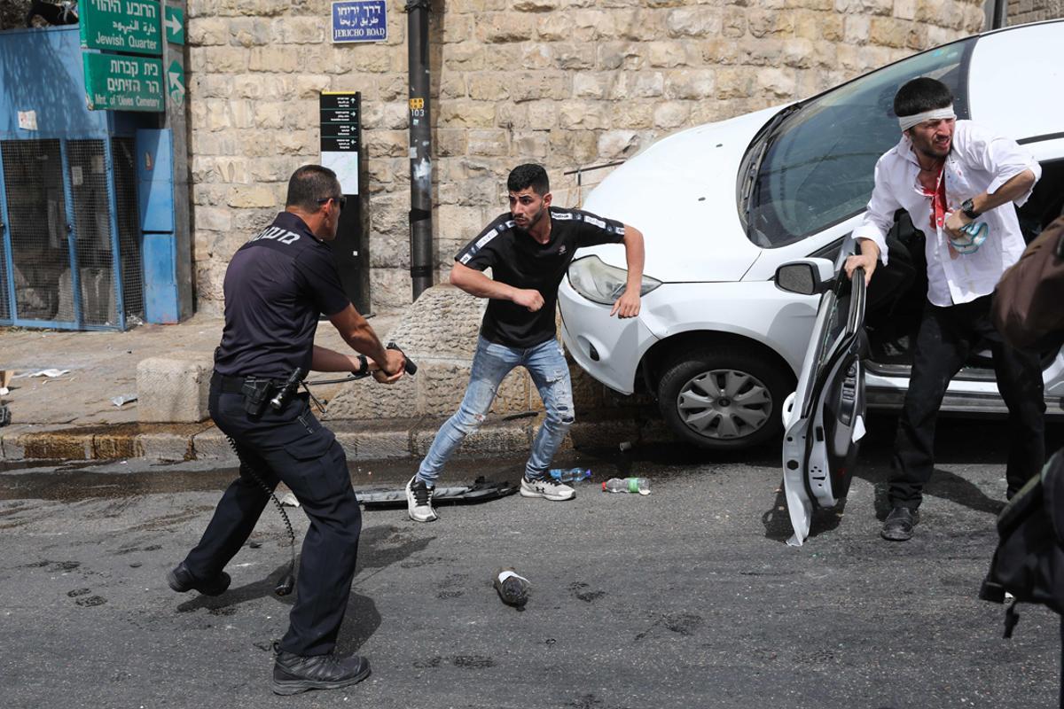 Un policía israelí apunta con un arma a un palestino junto a un judío ortodoxo herido que estrelló su coche cerca de la Puerta de los Leones.