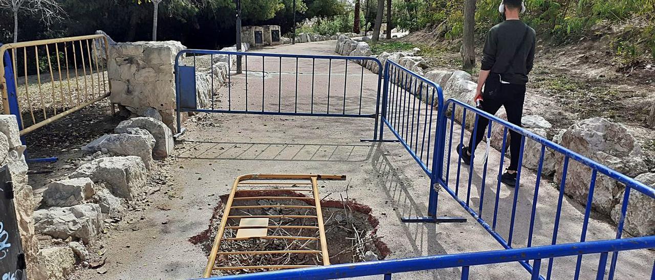 El socavón aparecido en uno de los caminos del parque y, a la derecha, escalera cerrada al paso y el muro resquebrajado al fondo. | L.G.L.