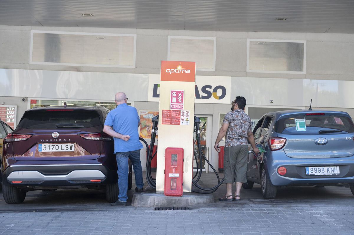 Dos hombres reposatn gasolina a sus coches en una gasolinera en la avenida Paral.lel, en Barcelona.